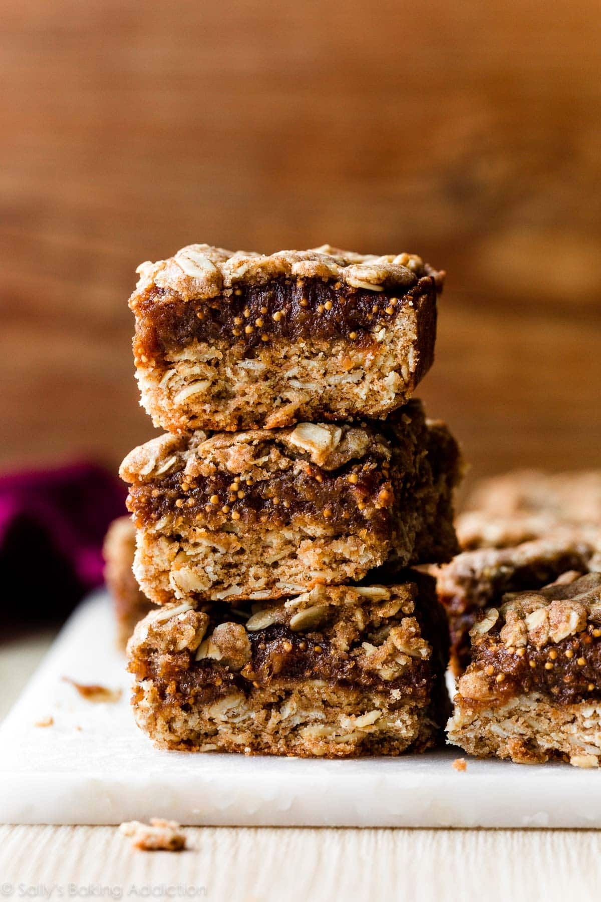 Stack of three oat and date bars on a white surface with a rustic wooden background