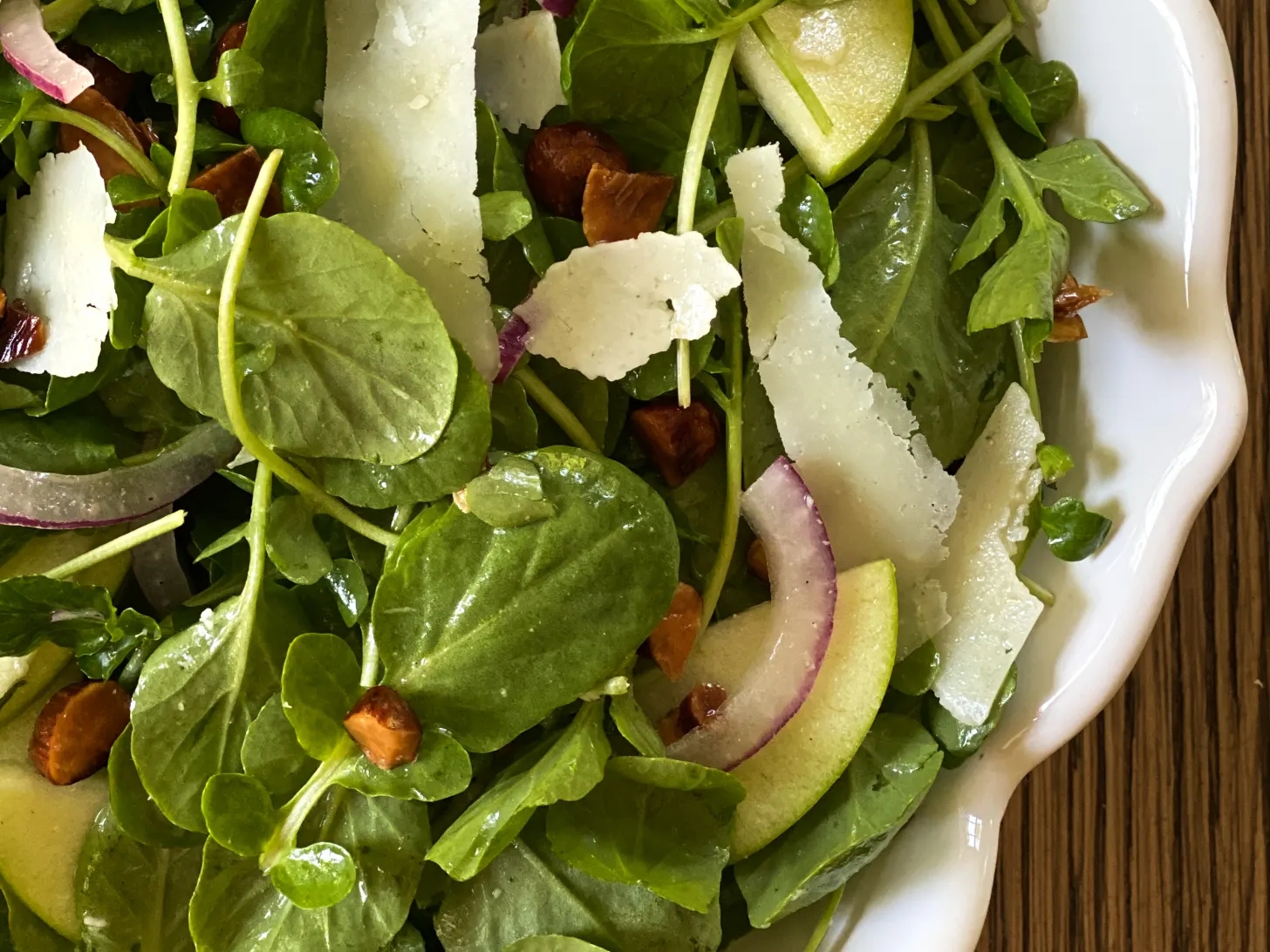 Salad with leafy greens, apple slices, red onion, cheese shavings, and almonds in a white bowl