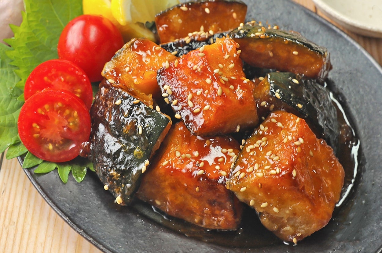 ごまがまぶされた焼きかぼちゃとトマトの料理が黒い皿に盛られている。