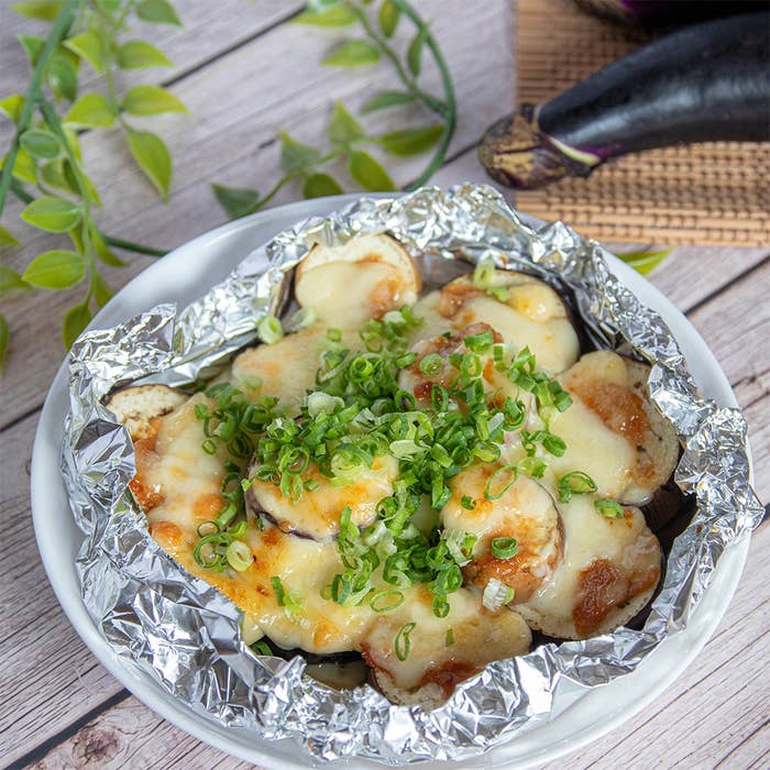 アルミホイルの上に焼かれたチーズとネギがトッピングされた料理。横になすがディスプレイされている。