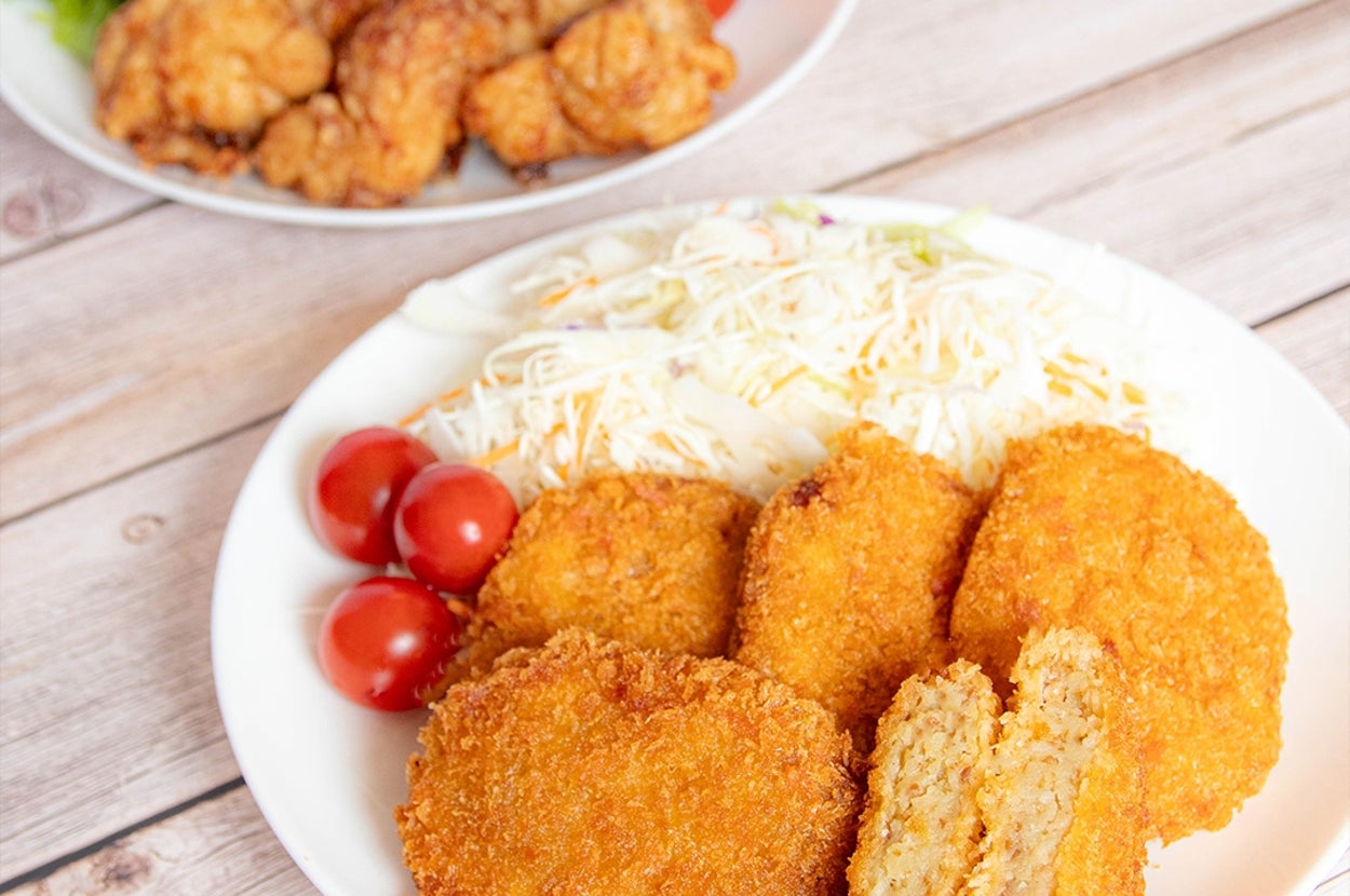 フライ盛り合わせの料理。メインはコロッケ、その横にサラダとトマト。背景に唐揚げとレモンのプレート。
