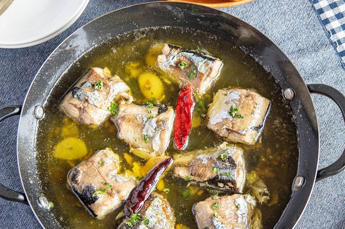 鍋に盛られた魚料理。にんにくや赤唐辛子が浮かび、おいしそうなアヒージョに仕上がっている。横にパンが添えられている。