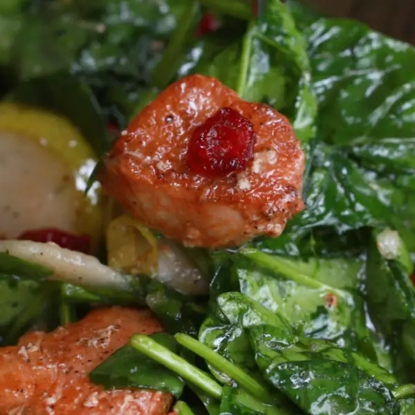 Chicken on a bed of fresh greens, topped with a dried cranberry, garnished with lemon slices and herbs