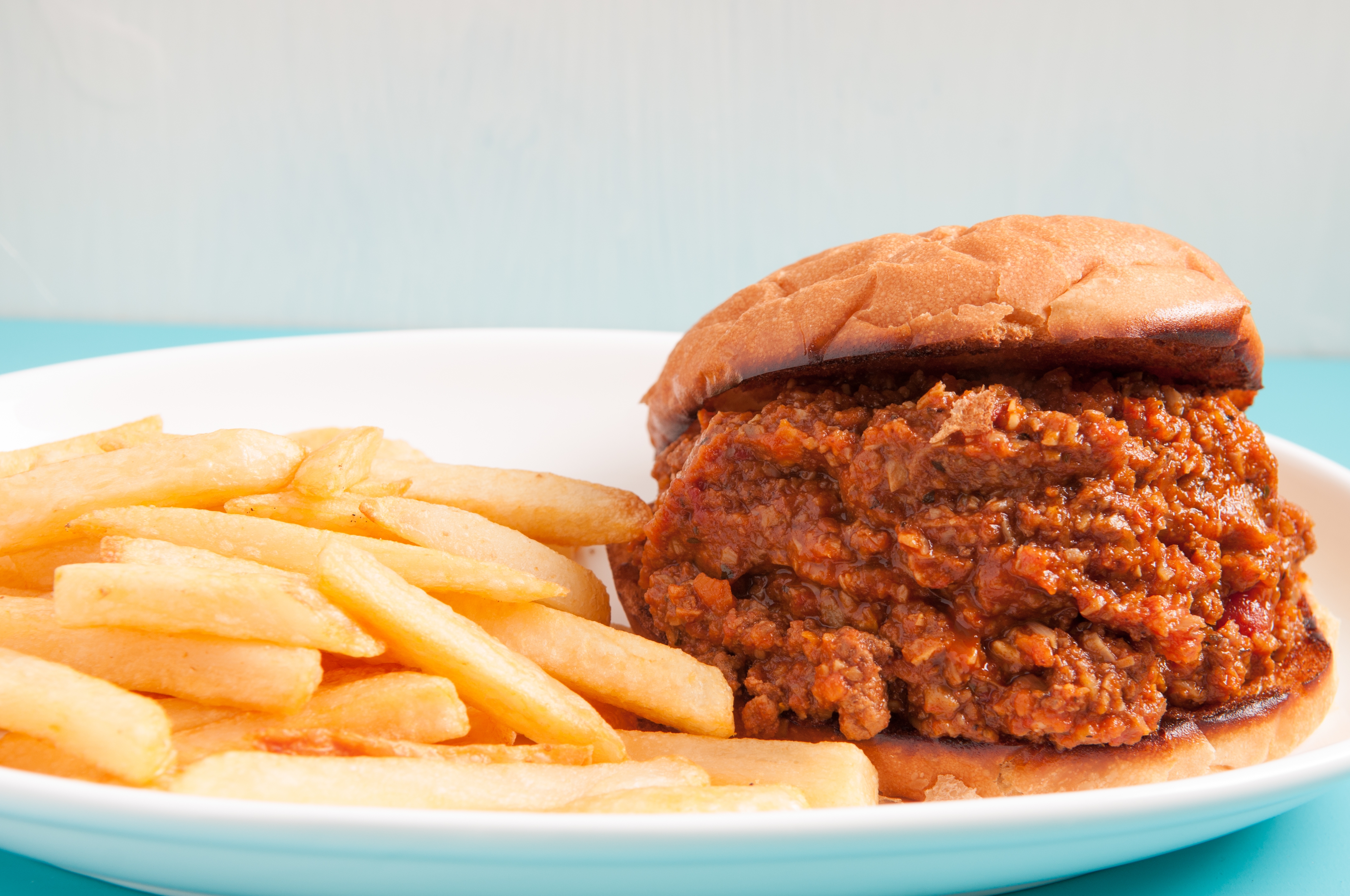 Sloppy joe sandwich with ground beef filling on a white plate, alongside a serving of French fries