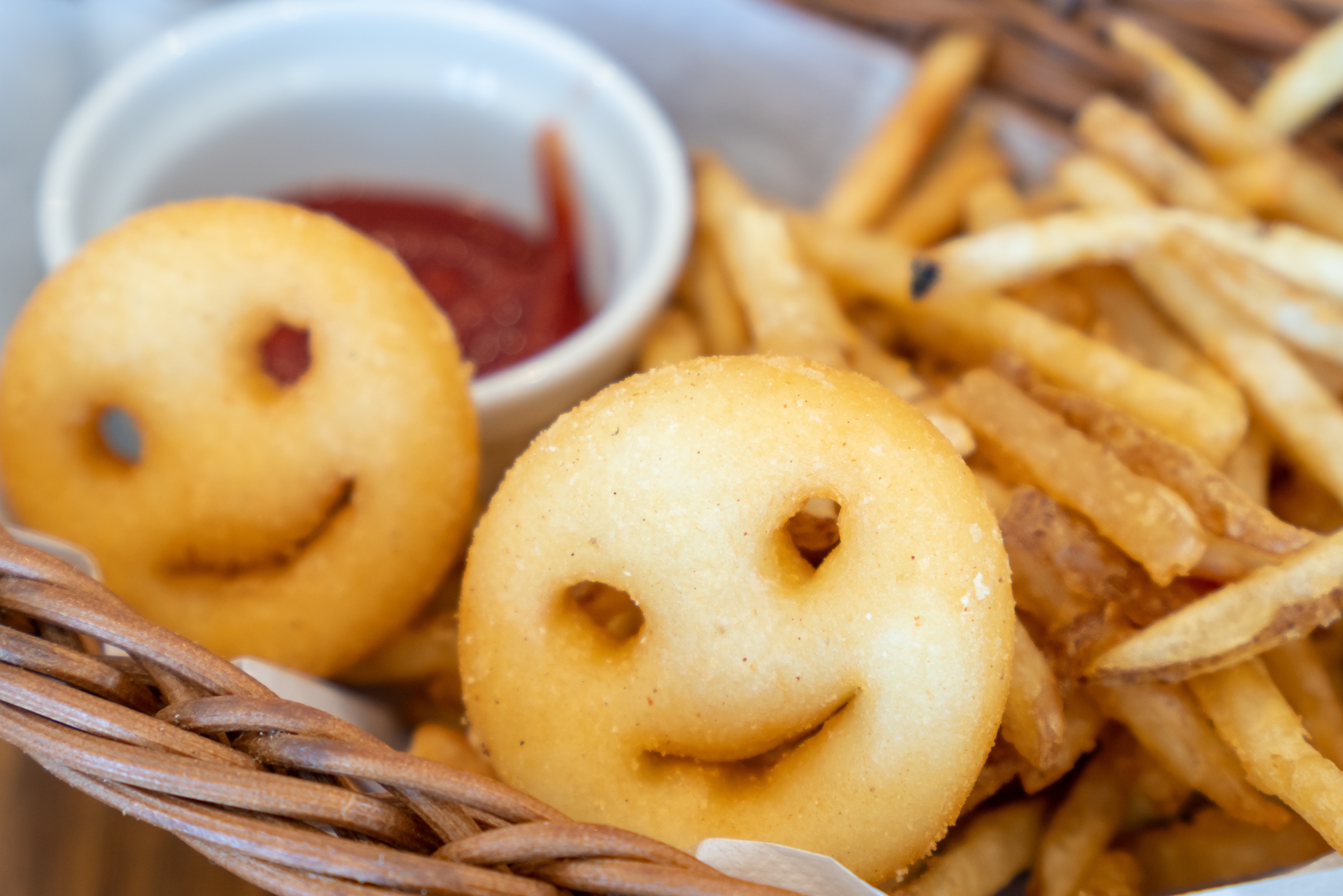 Smiley face fries and skinny fries in a basket with a small container of ketchup