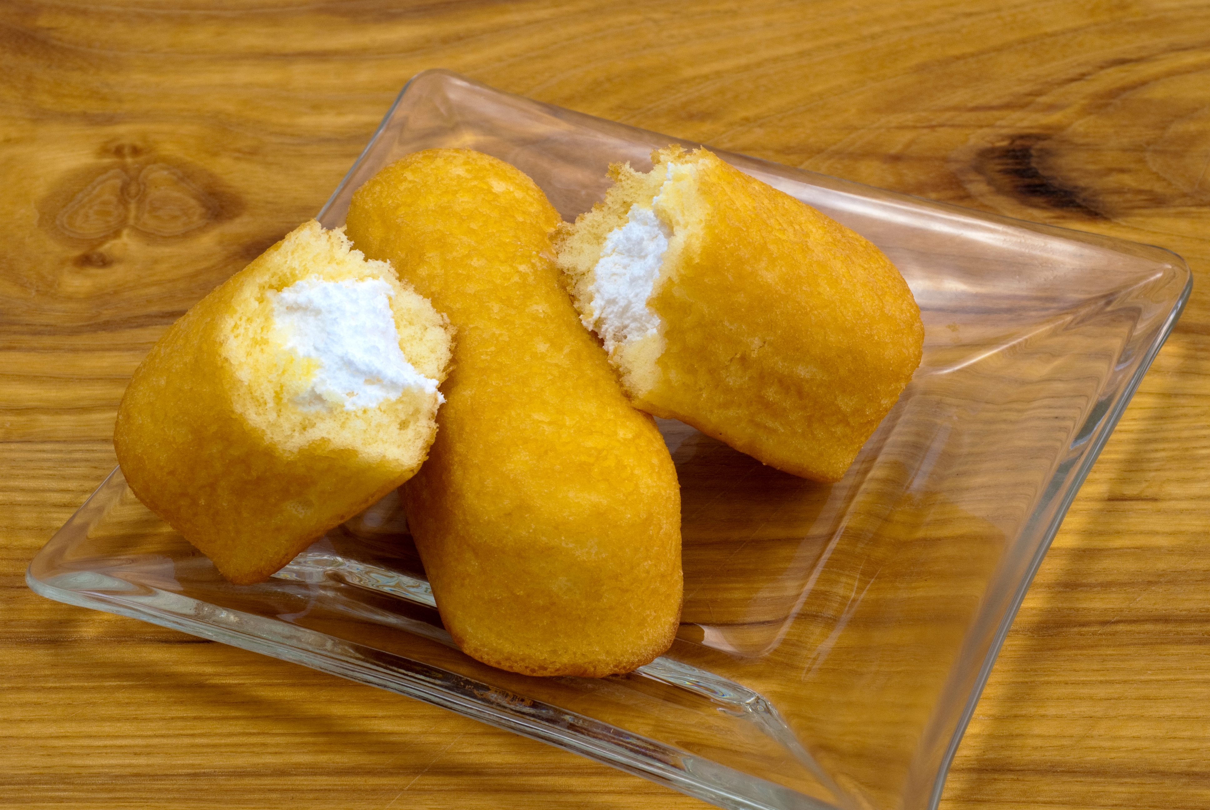 Three cream-filled sponge cakes on a glass plate, one cut in half to reveal the filling