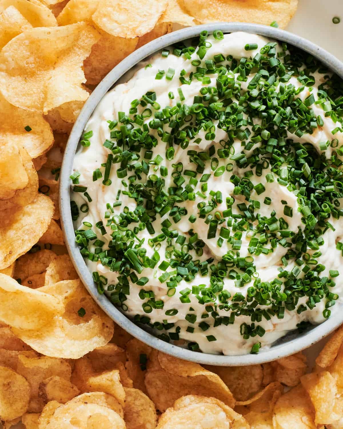 Bowl of creamy dip garnished with chopped chives, surrounded by crispy potato chips