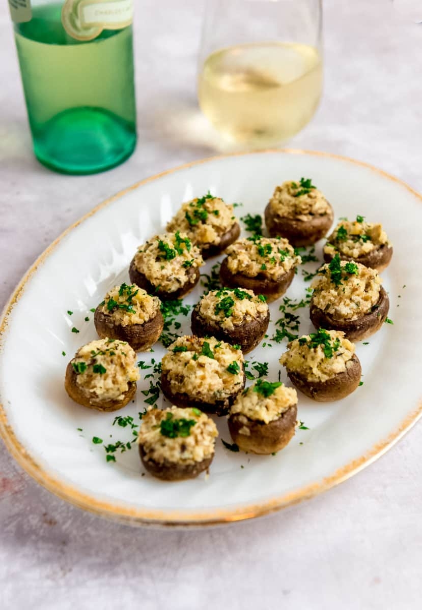 Stuffed mushrooms on a plate, garnished with parsley, next to a bottle and a glass of white wine