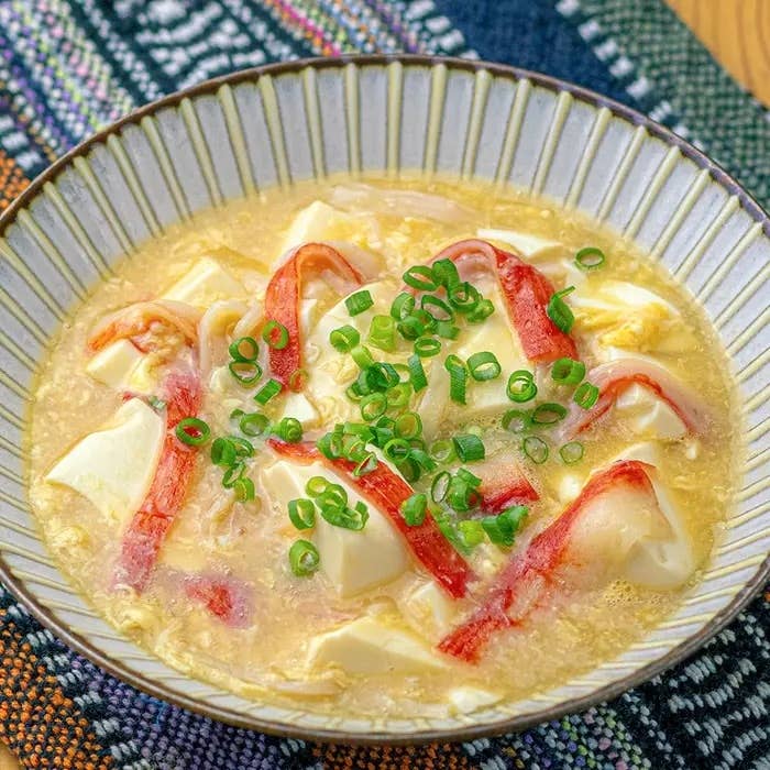 豆腐とかに風味かまぼこの卵とじ。豆腐とカニカマが入ったスープ皿、上に刻んだネギが散らされています。