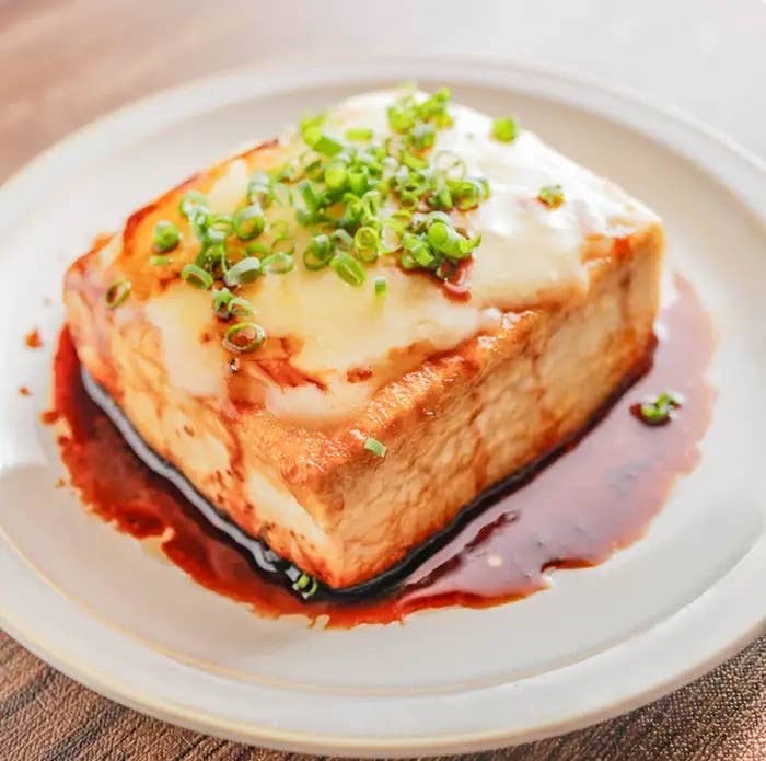 チーズ照り焼き豆腐。豆腐ステーキにソースがかかり、ネギがトッピングされた料理が白い皿に盛られている。