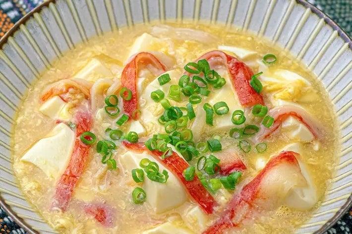 カニカマと豆腐が入ったスープのボウル。上に刻んだネギがトッピングされている。
