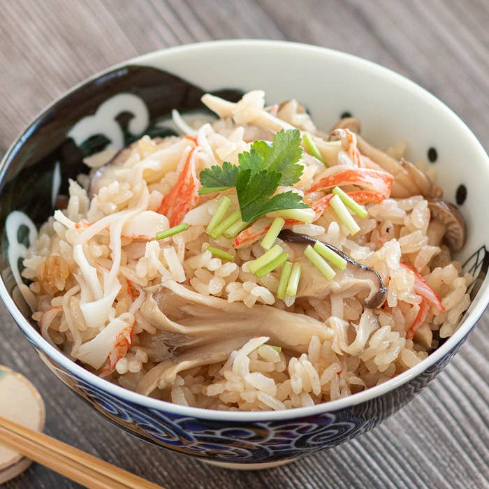 キノコとカニカマが乗った炊き込みご飯が和風の器に入っている。パセリが添えられている。