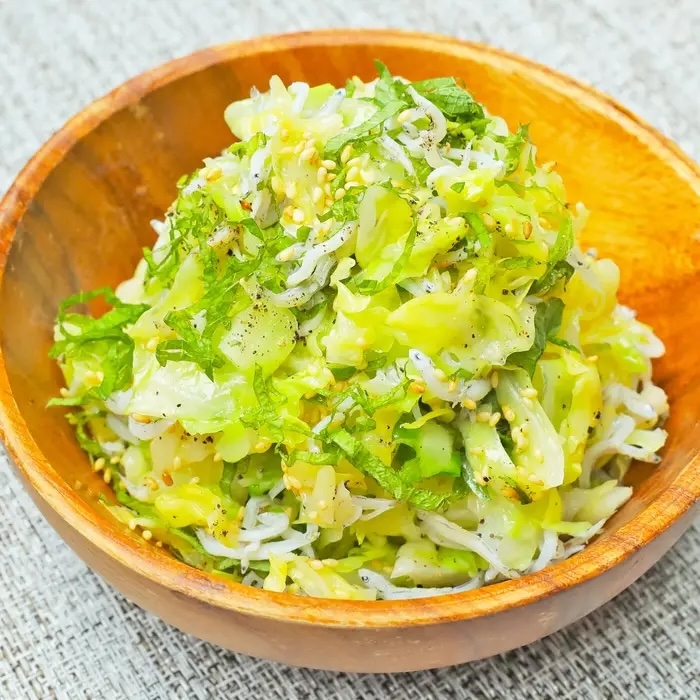 木製ボウルに盛り付けられた新鮮なキャベツとじゃこのサラダ。トッピングにゴマとハーブがのっている。