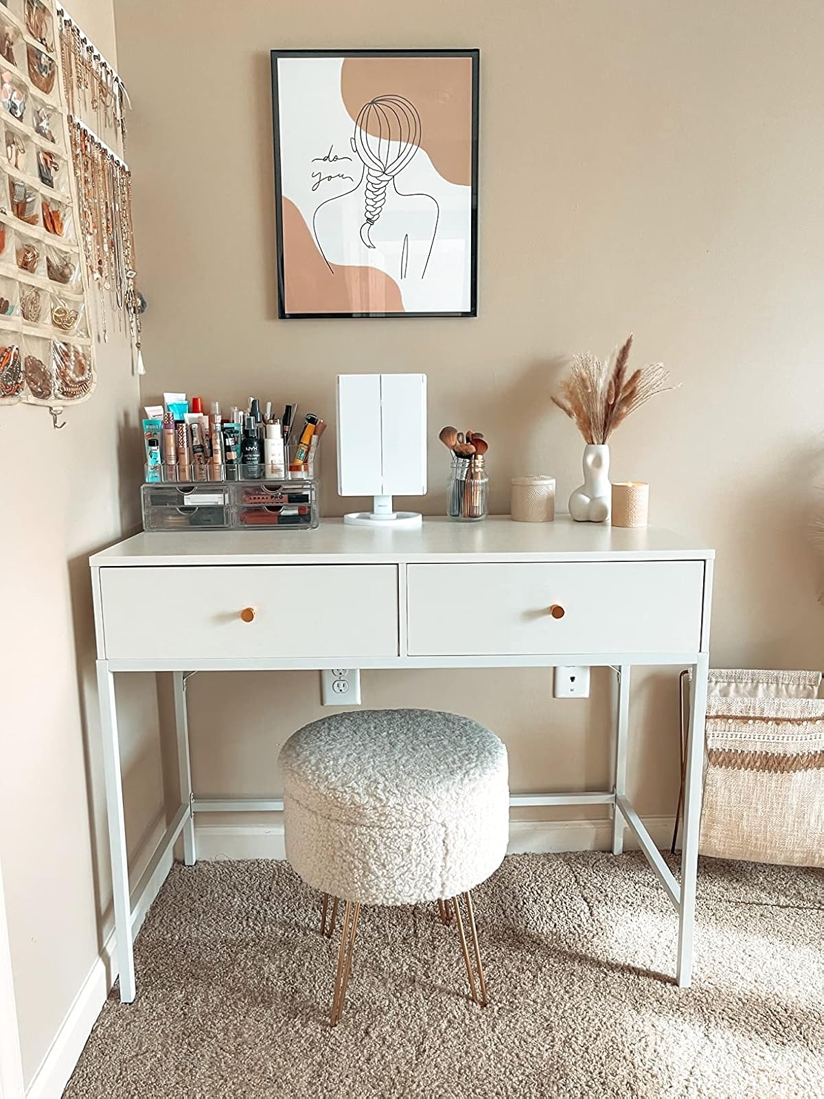 Chic makeup vanity with a framed minimalist art print above, makeup organizers, a mirror, and a plush stool in a cozy setup