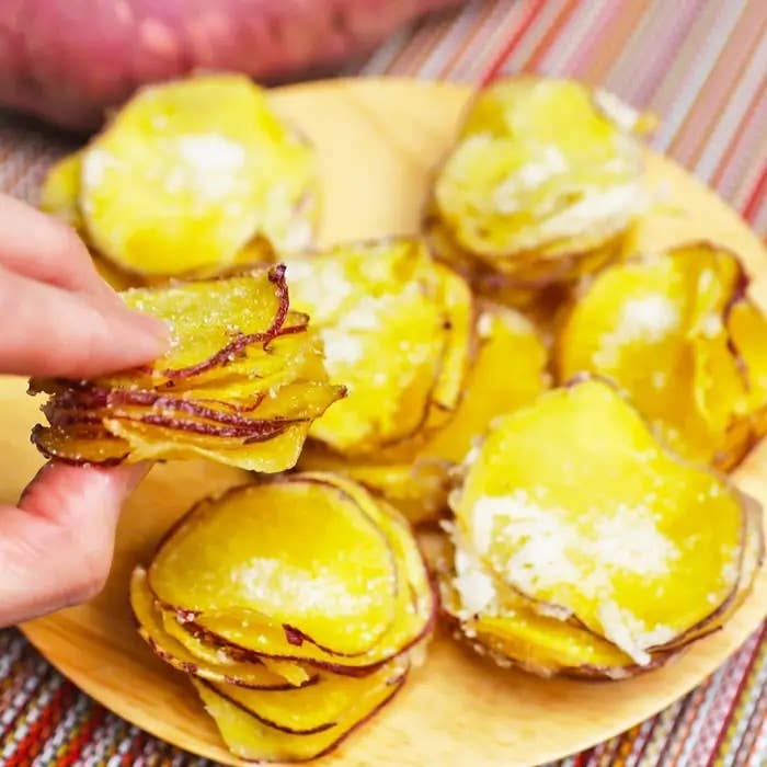 さつまいものミルフィーユ揚げ。手で持たれた、パルメザンチーズがかかったポテトチップの盛られた皿。