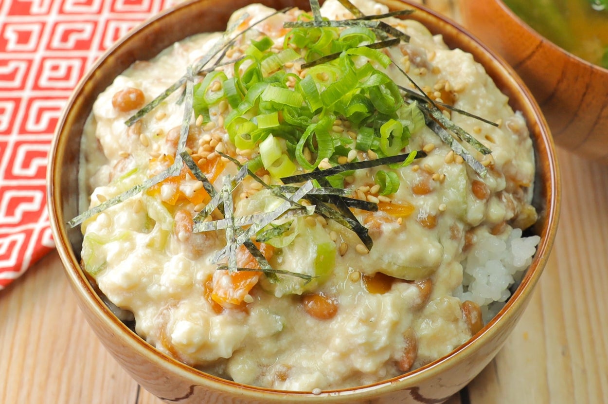納豆と山芋のとろろがけご飯が盛られた木製の器。味噌汁と布ナプキンが添えられている。