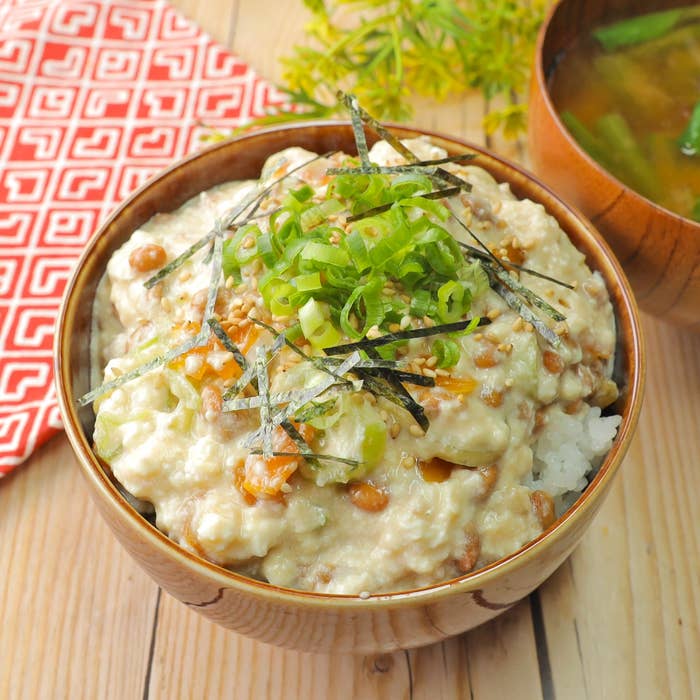 納豆ご飯が盛られた木製の器。味噌汁と布ナプキンが添えられている。