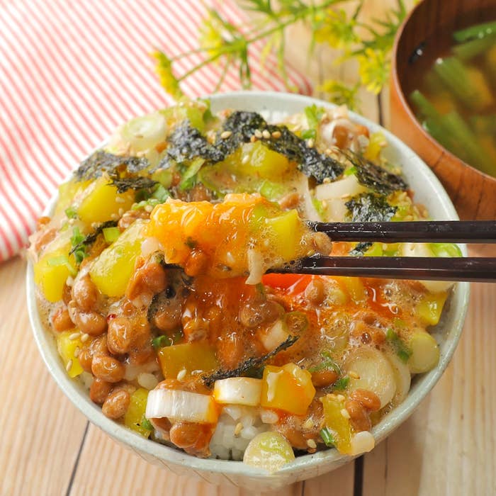 納豆、海苔、野菜をのせたご飯。箸で食べようとしている。ミソスープが横にある。
