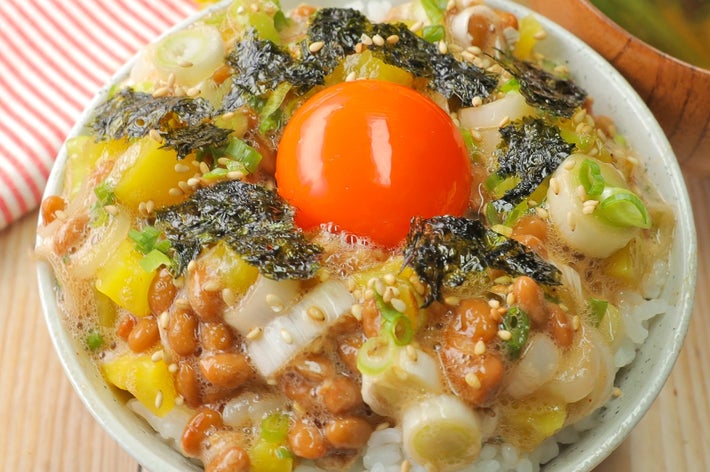 納豆、海苔、ネギ、卵黄がのったご飯の丼。そばに味噌汁。