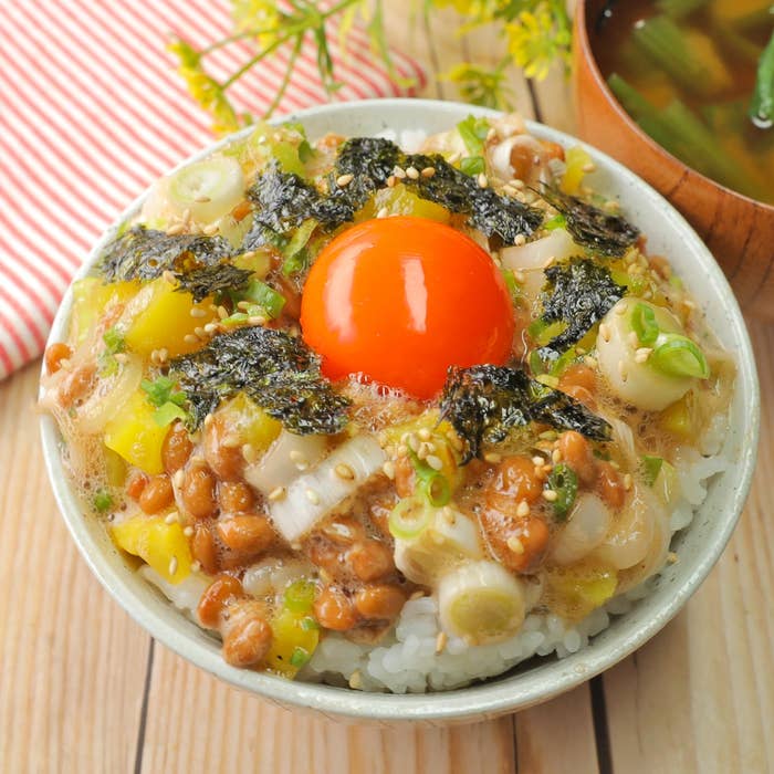 納豆、海苔、ネギ、卵黄がのったご飯の丼。そばに味噌汁。