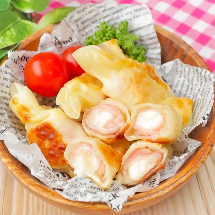 お皿に盛られたチーズとハムを使った料理、横にプチトマトとパセリが添えられている。