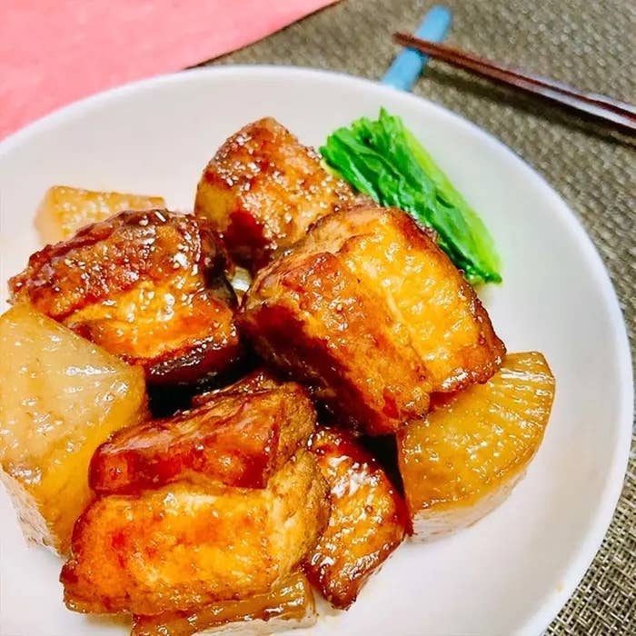 豚の角煮が白い器に盛られている。隣には青菜と大根が添えられており、箸が横に置かれている。