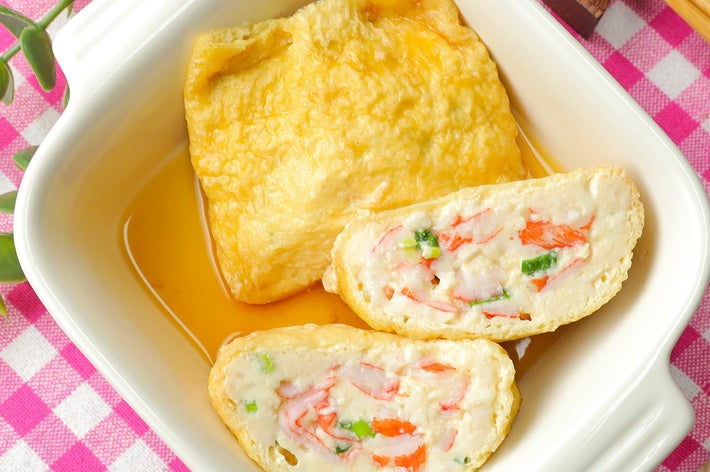 豆腐と野菜が詰まった揚げ包みが白い皿に盛られている。横に割った断面が見える。ピンクのチェック柄が背景にある。
