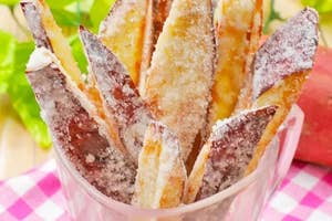 ガラスのコップに入った砂糖がけのフライドスイートポテト。背景に緑の葉とチェック柄のクロスが見える。
