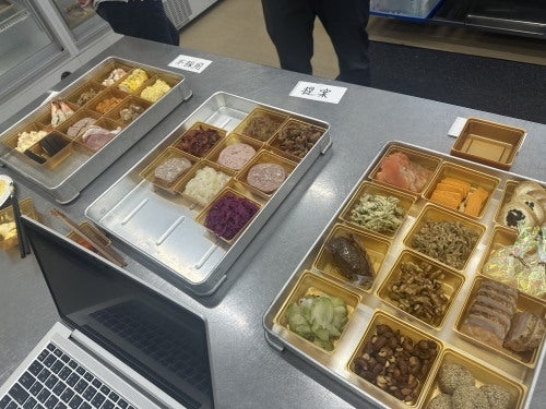 机の上に弁当が並び、仕切られた容器に多様な料理が盛り付けられている。