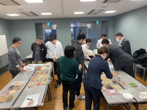 人々がテーブルで食べ物の準備をしているビジネスミーティング。数名がカジュアルで、他はスーツを着用。