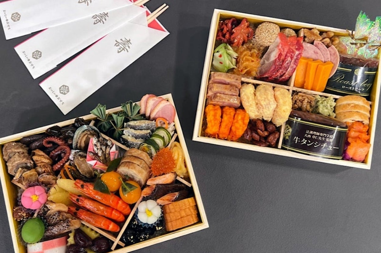 豪華なおせち料理が二つの重箱に詰められている。左側は海老などの魚介類、右側は肉や野菜などが盛り付けられている。