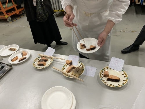 料理コンテストの審査員が、紙皿に盛られた食品を箸で味見している。