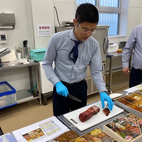 男性が厨房で肉を切り分けている様子。作業台には様々な料理が並んでいる。