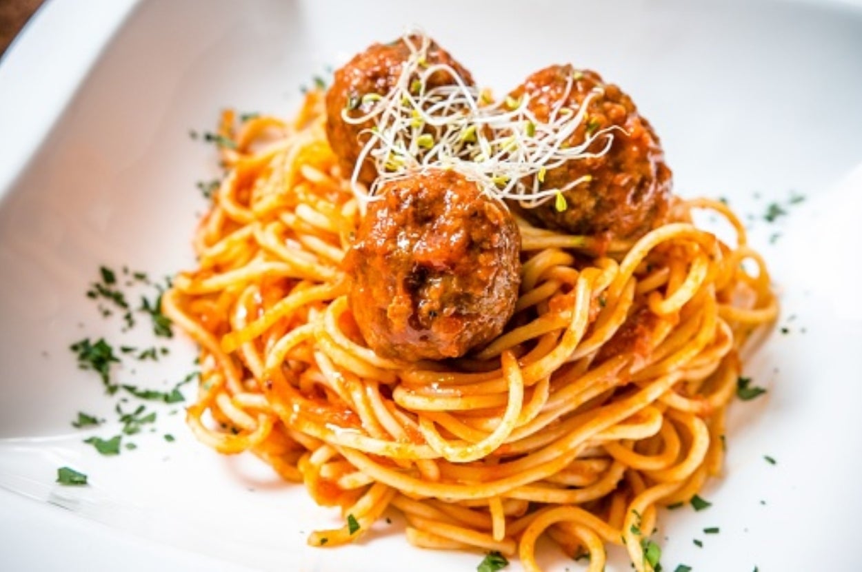 Spaghetti with tomato sauce and meatballs topped with sprouts, garnished with fresh herbs on a white plate