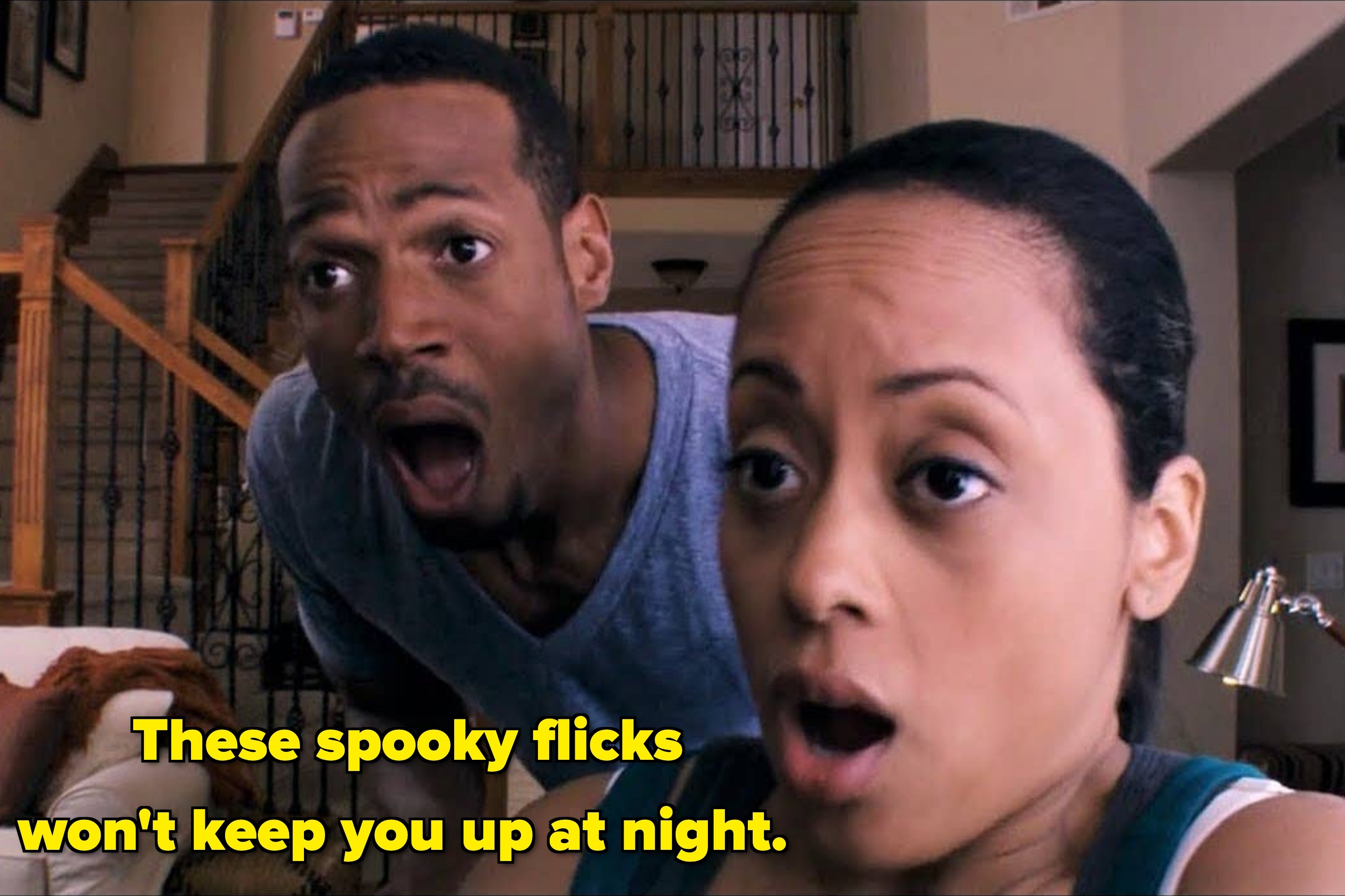 A man and woman with shocked expressions sit in a living room, reacting to something off-screen