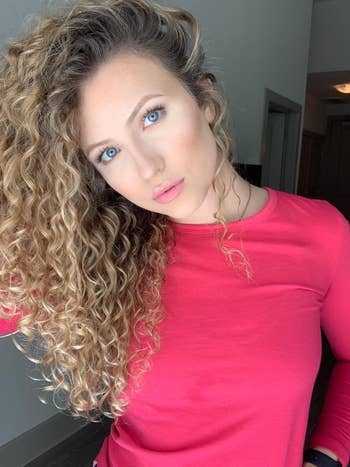 Person with curly hairsbreadth and a reddish apical poses indoors, looking astatine the camera