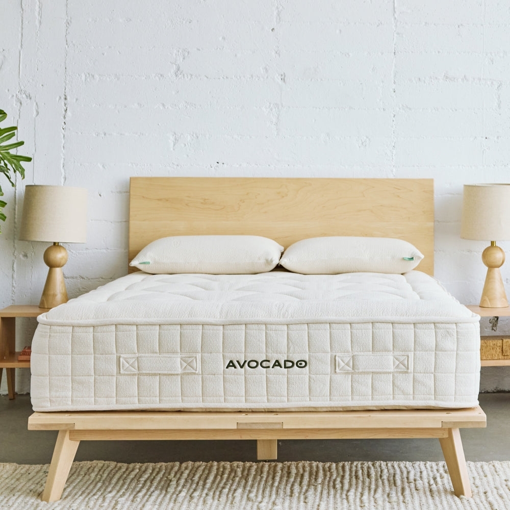 Avocado mattress on a minimalist wooden frame, flanked by lamps, against a textured white wall