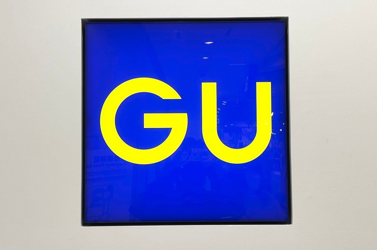 Sign with large yellow letters "GU" on a blue background within a square frame on a wall