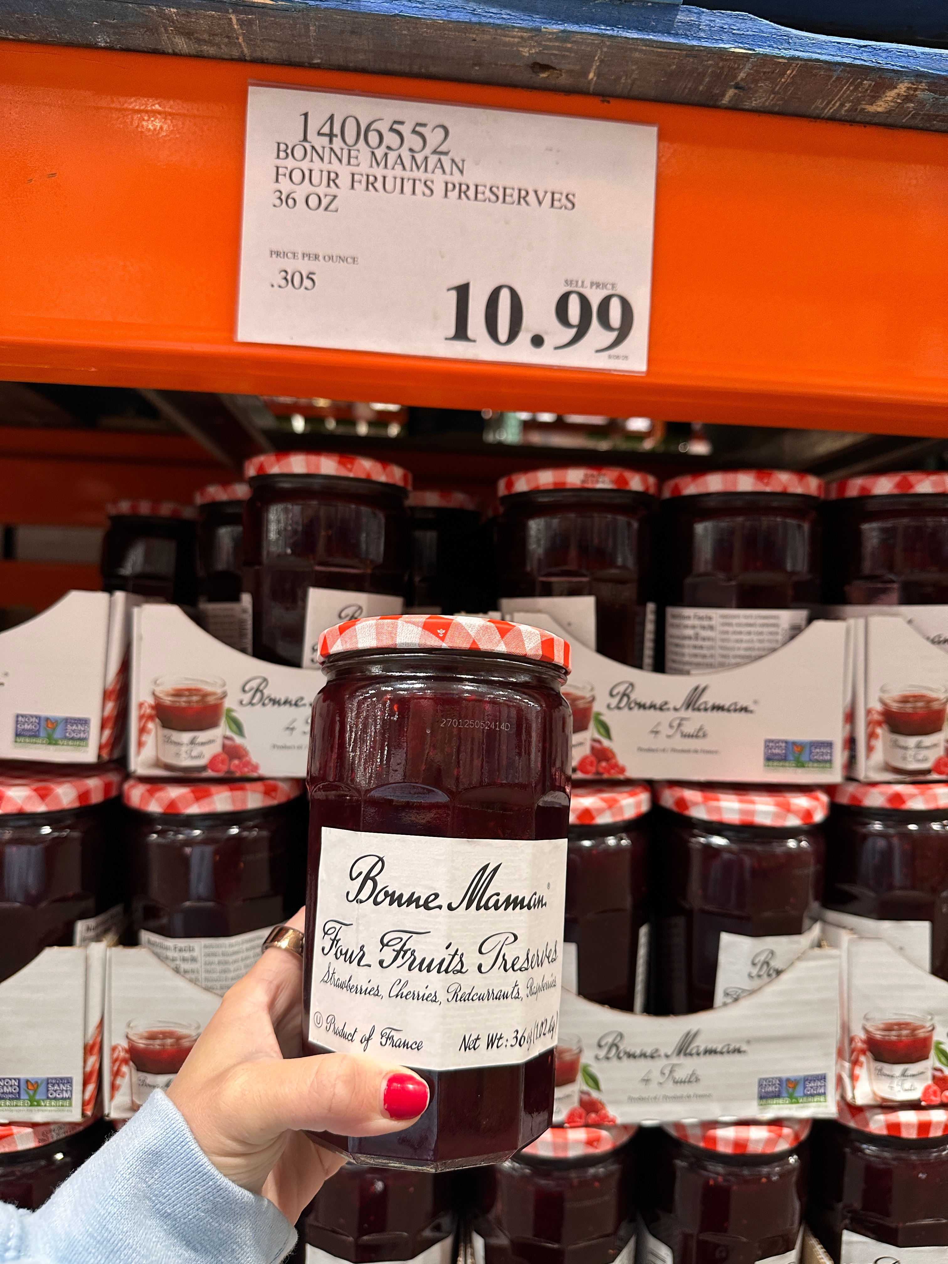 A hand holds a jar of Bonne Maman Four Fruits Preserves in a store, with a shelf full of jars and a price tag of $10.99 visible