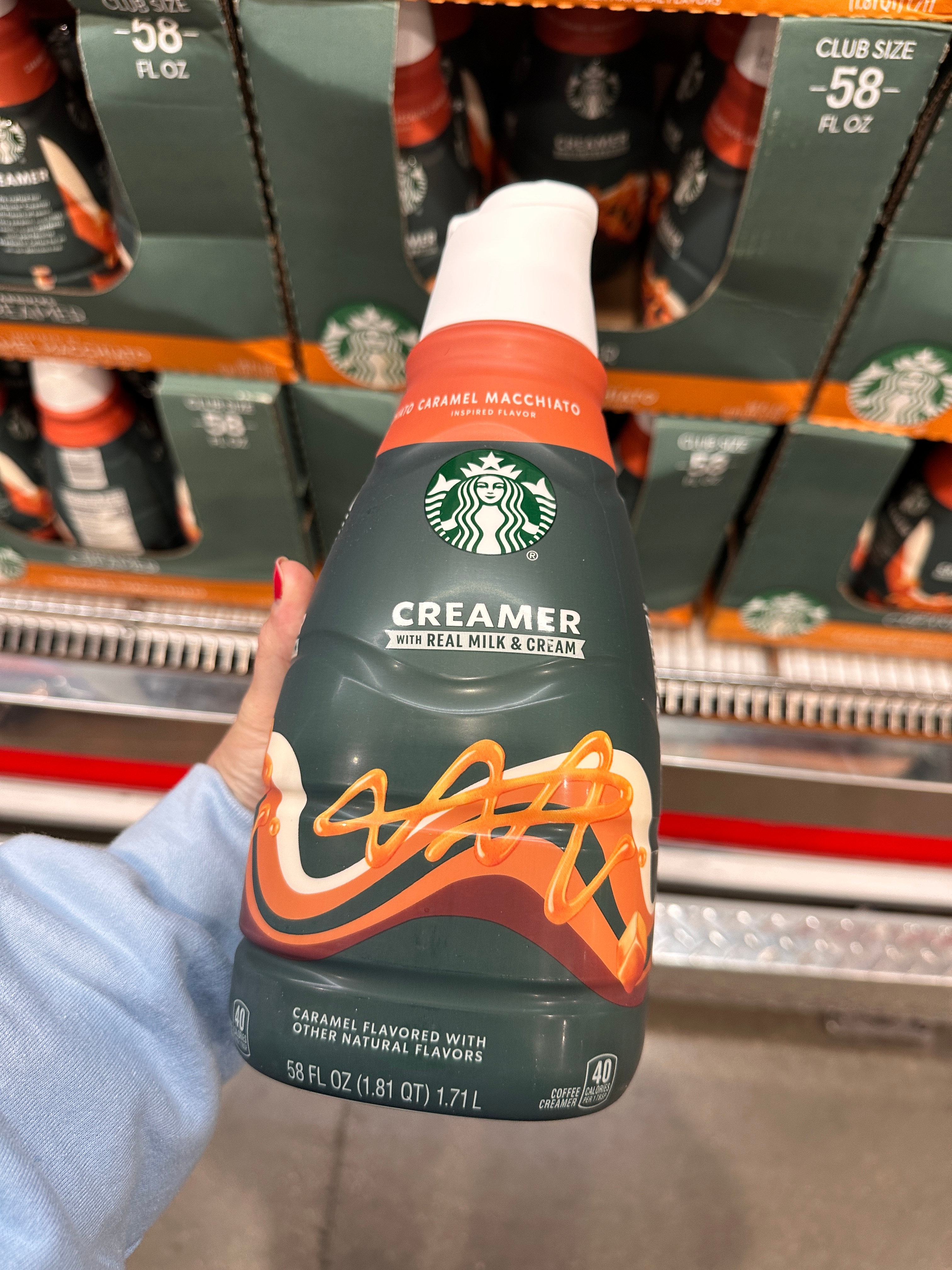 Person holding a Starbucks caramel macchiato creamer bottle in a store aisle