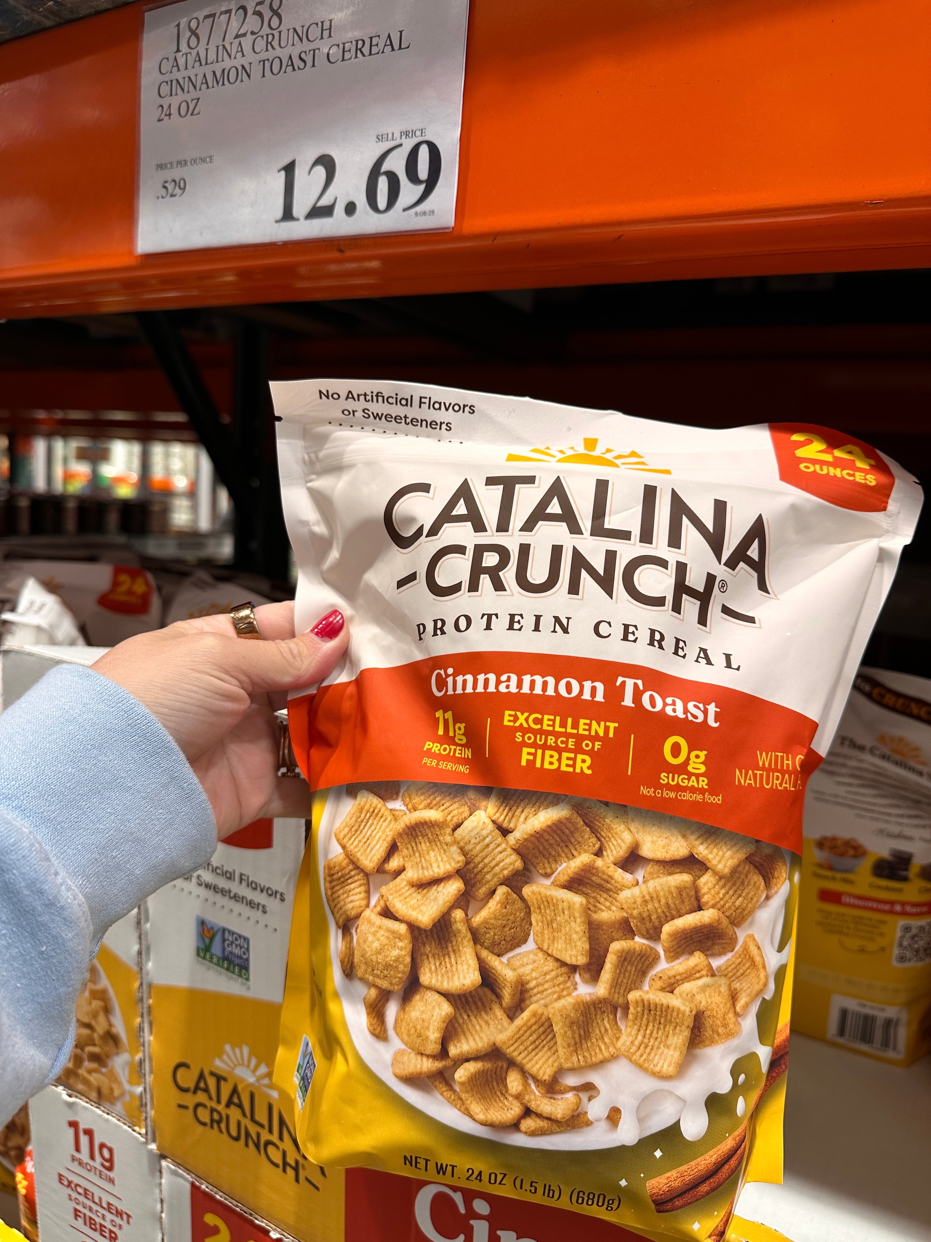 Person holding a bag of Catalina Crunch protein cereal, cinnamon toast flavor, in a store. Price tag above reads $12.69