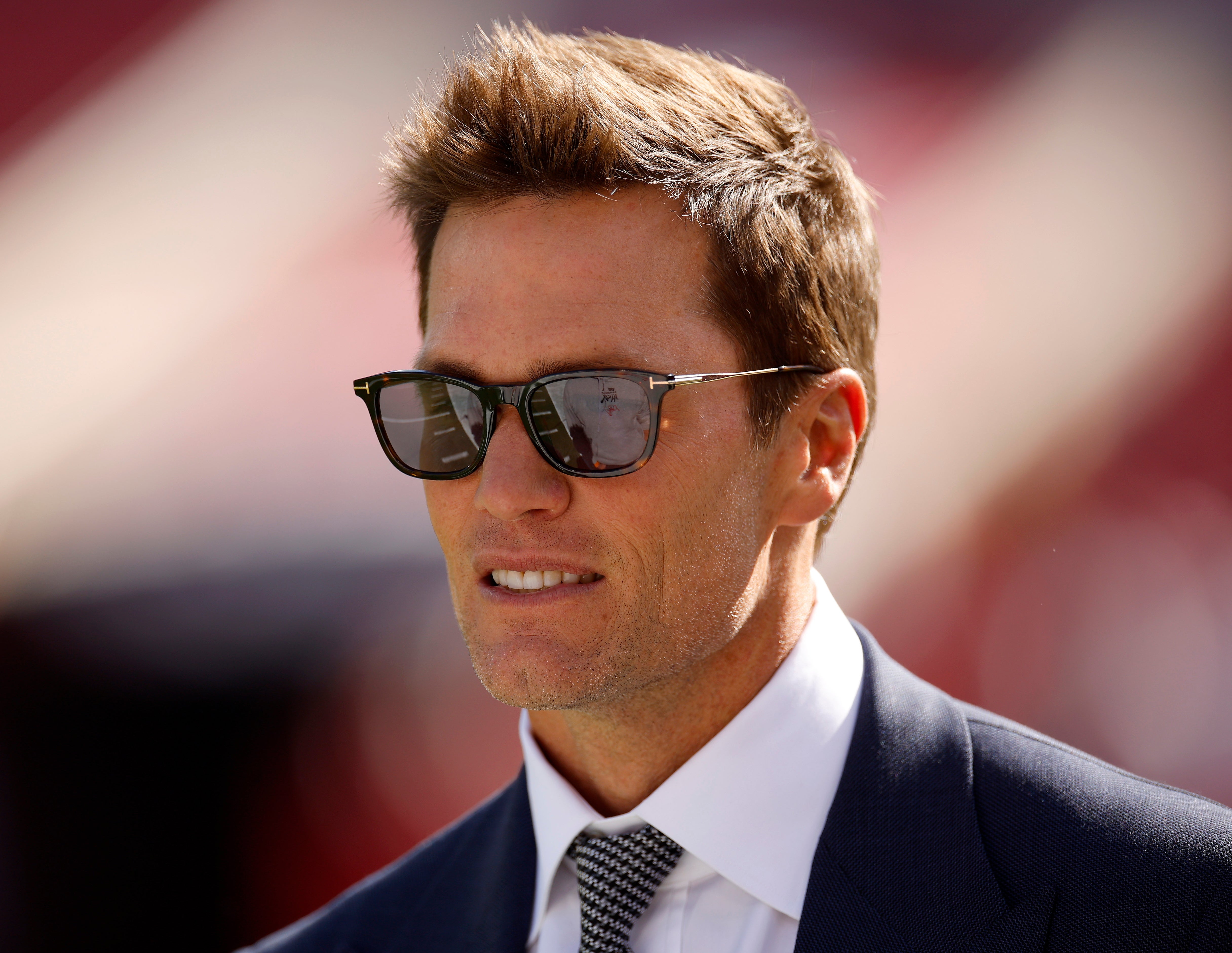 Tom Brady in sunglasses and a suit at an outdoor event