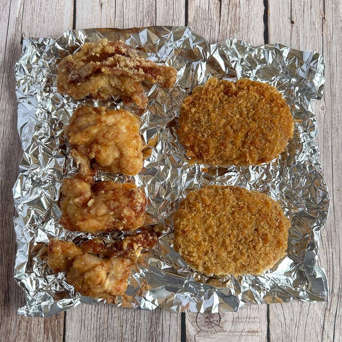 アルミホイルの上に鶏の唐揚げと2枚のコロッケが置かれたシンプルな食事の写真です。
