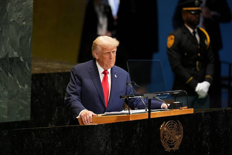 A person stands at a United Nations podium, delivering a speech, with security personnel in the background