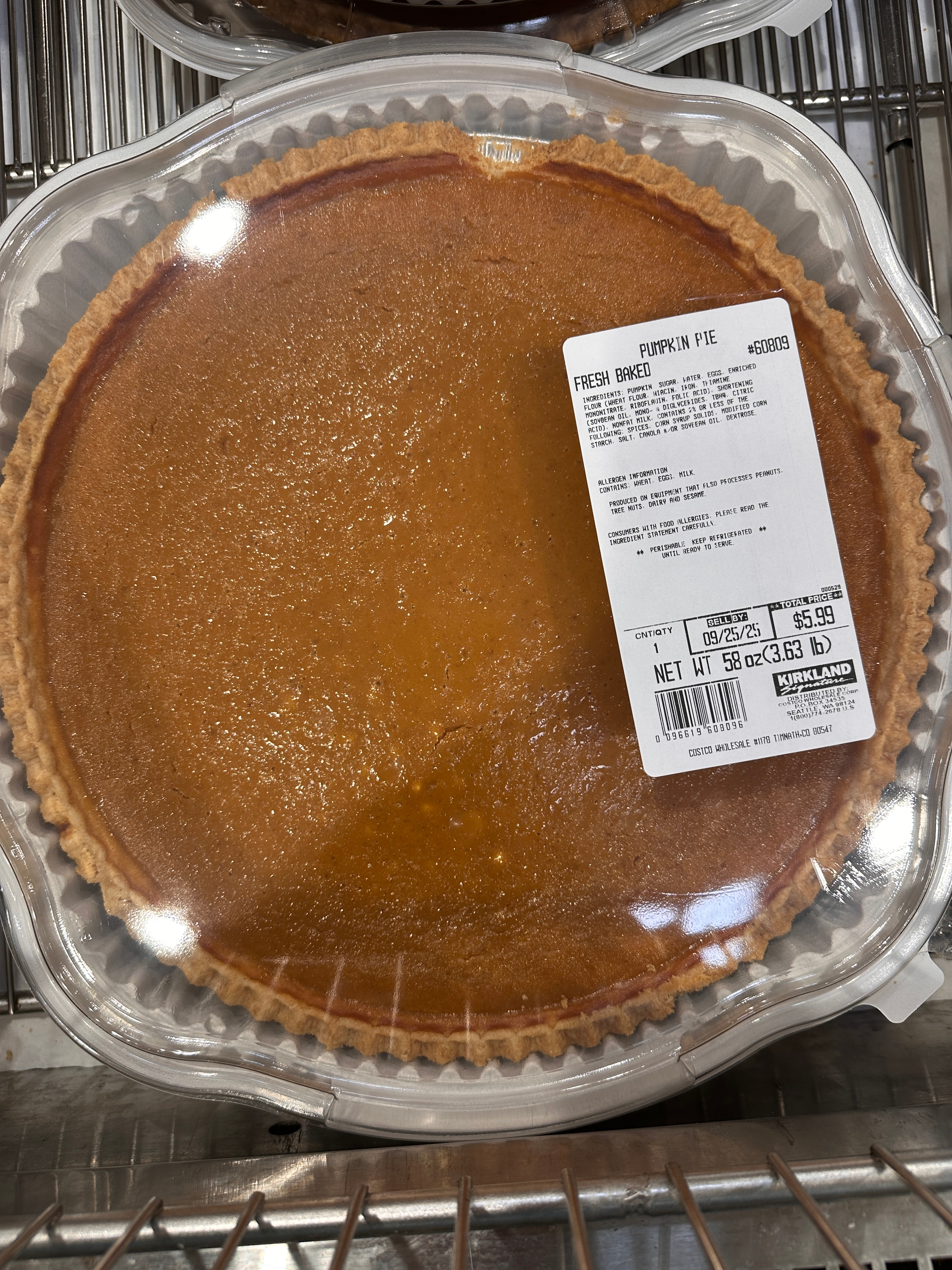 Pumpkin pie in a clear plastic container with a price label on top, displayed on a metal shelf
