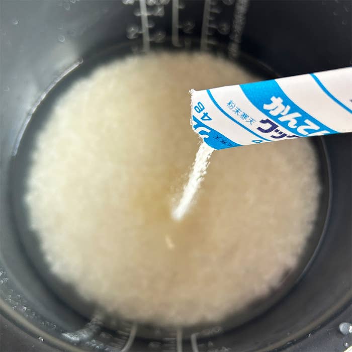炊飯器に白い粒状の粉を注いでいる様子。