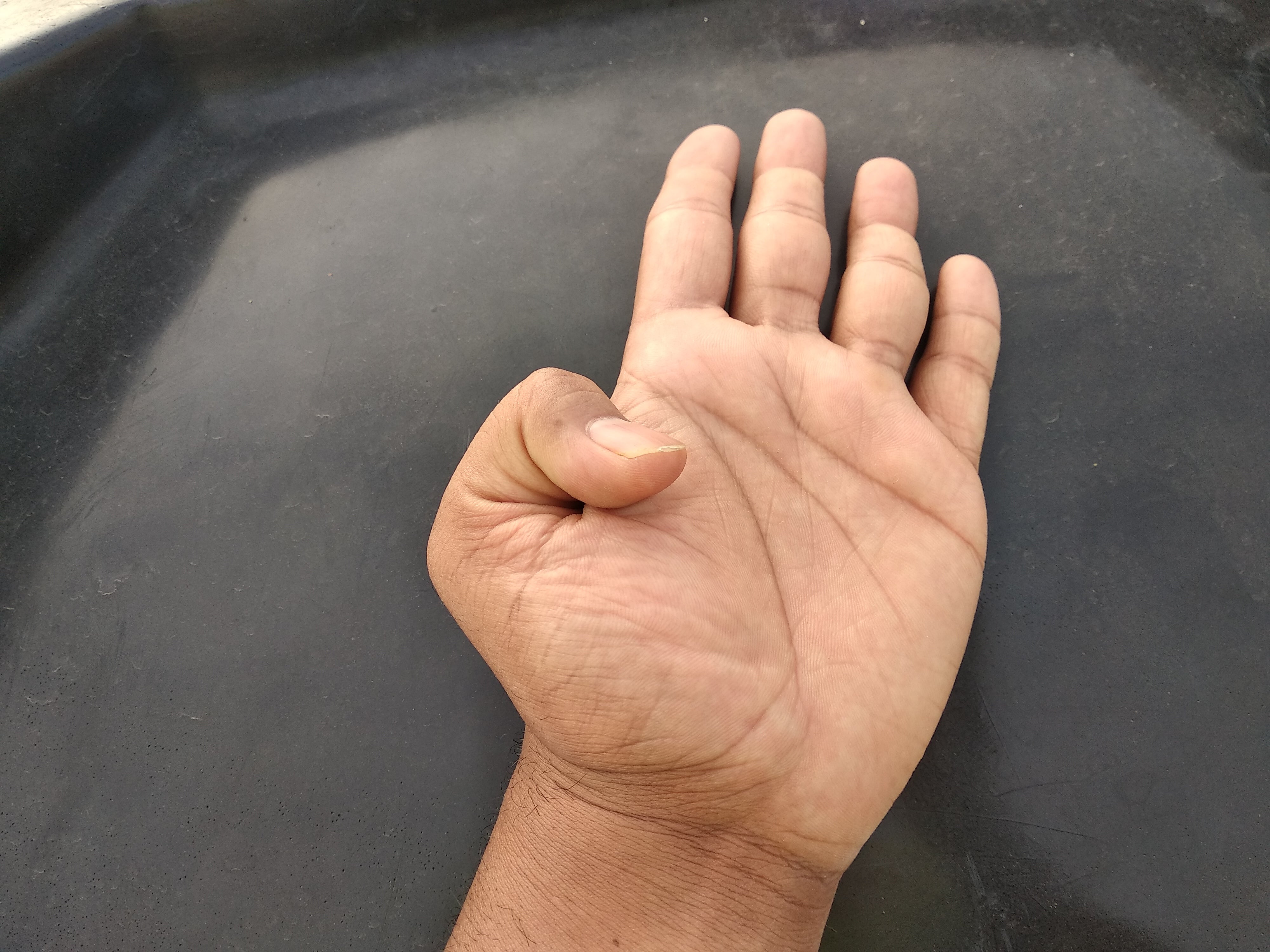 En hånd som viser hitchhiker's tommel, hviler på en mørk overflate med fingrene litt spredt