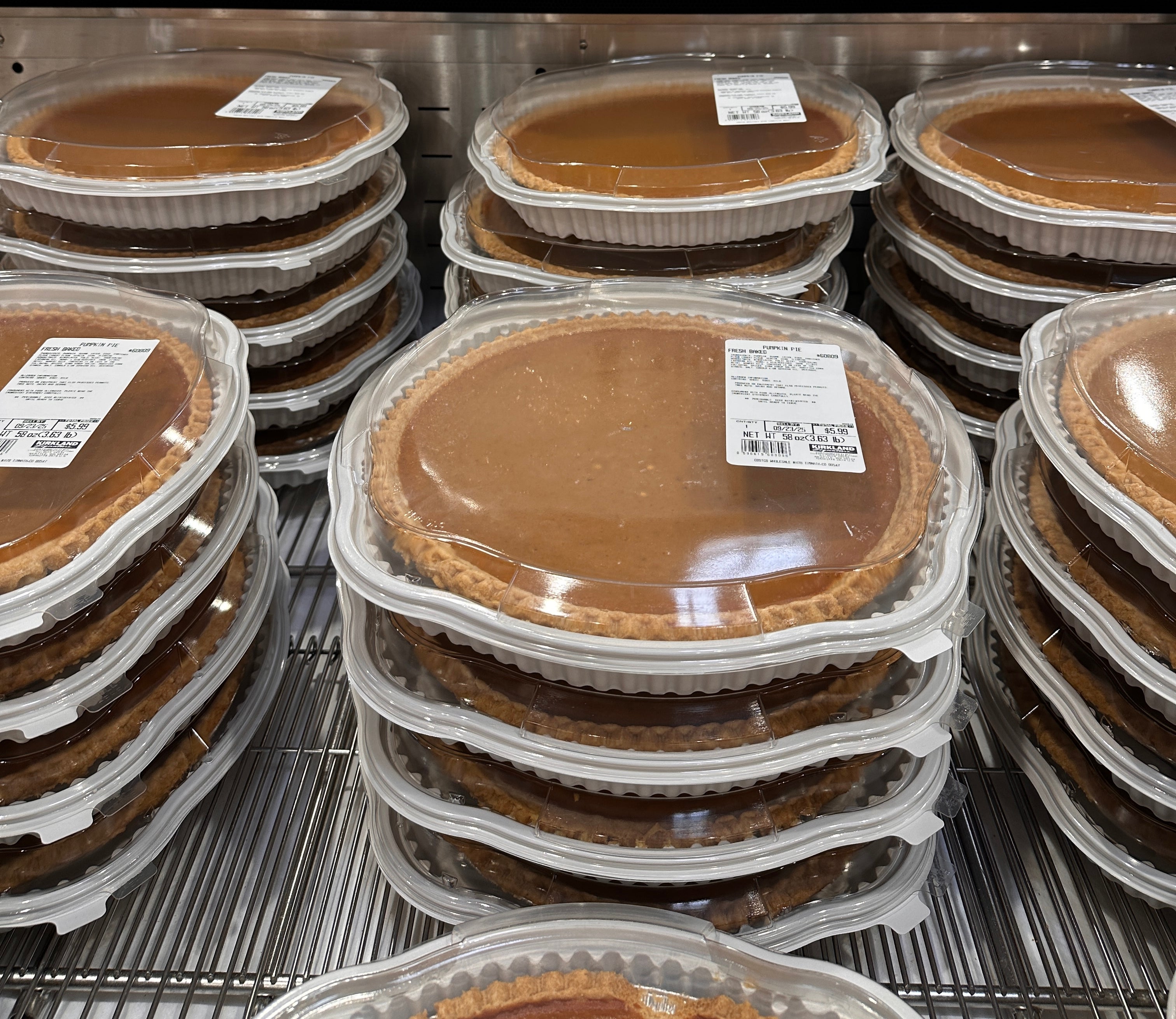 Pumpkin pies in plastic containers stacked on a store shelf. Price above: $5.99 each for a 58 oz pie