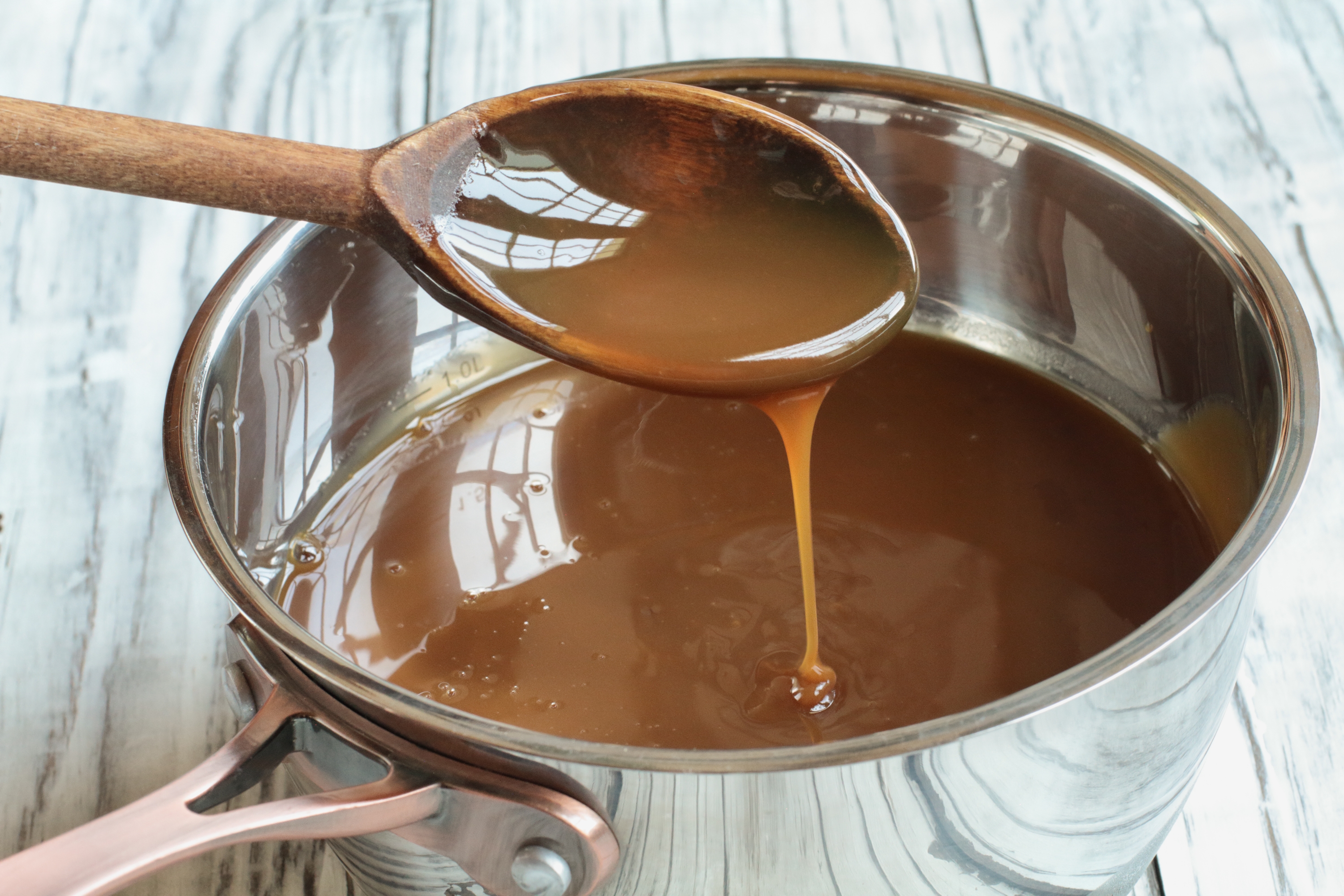 Caramel sauce being stirred with a wooden spoon over a saucepan, ready to serve