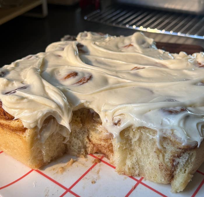 A freshly baked cinnamon roll slab with creamy frosting on a plate, missing a few pieces, ready to enjoy